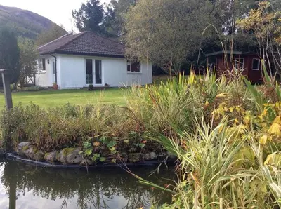 a white house with a garden in front of the water at Dalkell Cottages in Tyndrum