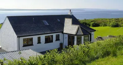 a house on a hill with the ocean behind it at Portbahn, Bruichladdich in Bruichladdich