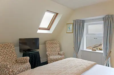 a bedroom with a bed and a chair and a window at Kilchrenan House in Oban