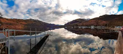 a view of a river with a reflection of the mountains at Bonnie Banks Lodge Ardlui in Ardlui