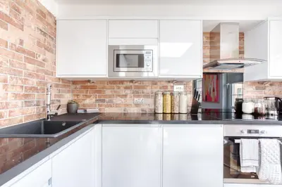 a kitchen with white cabinets and a brick wall at Central Bright 3 Bed Flat with Pool & Parking in Edinburgh