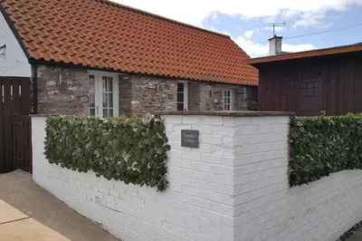 a white brick wall with ivy on it next to a house at Thornhill Lodge, Historic 4 Bed, 4 Ensuite in Stirling