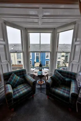 a living room with two couches and a table and windows at Burnside Guest House in Ayr