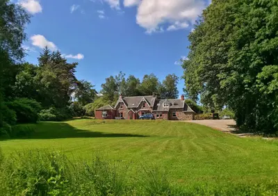 a large house on a green field with trees at The West Highland Way Campsite & Campervan Accommodation in Milngavie
