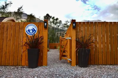 a wooden fence with a gate with two plants at Coe Pod, West Highland Way Holidays in Kinlochleven