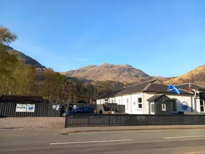 a building on the side of a road with mountains in the background at Coe Pod, West Highland Way Holidays in Kinlochleven