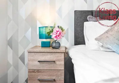 a bed with a nightstand with a vase of flowers on it at Anderson Apartment by Klass Living Motherwell in Motherwell