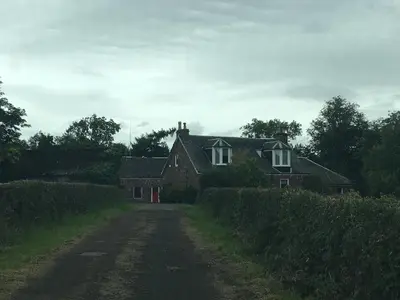 a house on a dirt road next to a field at Whiteley’s Cottages studio in Dumbarton