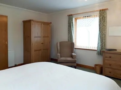 a bedroom with a bed and a chair and a window at Lismore Cottage in North Ballachulish