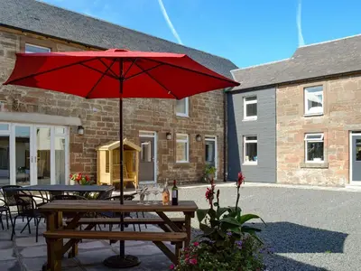 a picnic table with a red umbrella on a patio at Smithfield House in Tarbolton