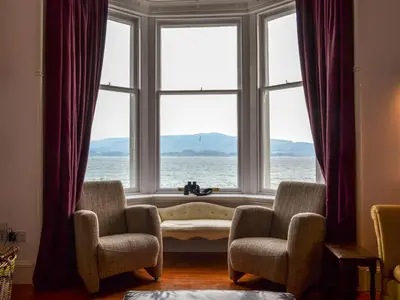 a window with a view of the ocean with two chairs at Fircliff - The House On Bute in Port Bannatyne