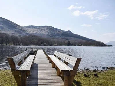 a wooden dock on a lake with mountains in the background at Lochearnside Lodge in Saint Fillans