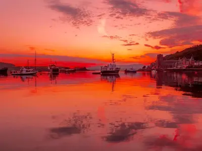 a sunset over a harbor with boats in the water at Finlaggan Apartment in Oban