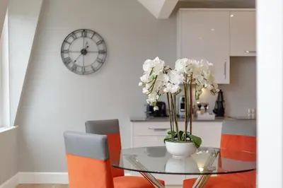 a dining room table with orange chairs and a clock at Destiny Scotland Hanover Apartments in Edinburgh