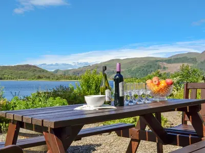 a wooden picnic table with a bottle of wine and glasses at Dunyvaig in Colintraive