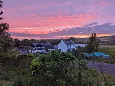 a white house in a field with a sunset at Glen Bay - 2 Bed Lodge on Friendly Farm Stay with Private Hot Tub in New Cumnock
