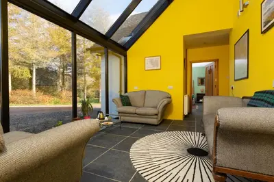 a conservatory with a yellow wall and chairs and a table at Powdermills B & B in Inveraray
