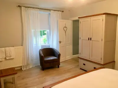a bedroom with a chair and a cabinet and a window at South Doll Farm Cottage in Airth