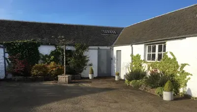 a white house with a garage and plants at South Doll Farm Cottage in Airth