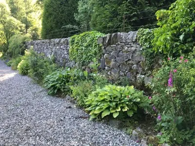 a stone wall and some plants and flowers at Mews Cottage Ardoch Lodge Strathyre in Strathyre
