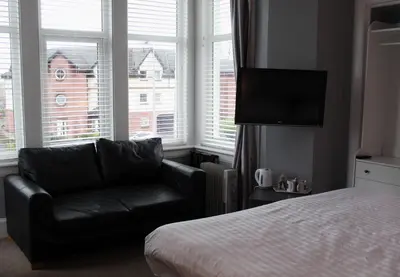 a bedroom with a couch and a bed and windows at The Woodhouse Hotel in Largs