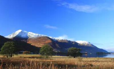 a mountain range with a lake and trees in the foreground at Arivonie Lochside Cottage in Glencoe