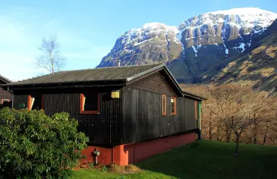 a house with snow covered mountains in the background at Birch Chalet in Ballachulish