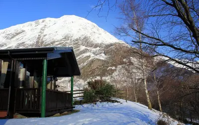 a snow covered mountain behind a building in the snow at Birch Chalet in Ballachulish