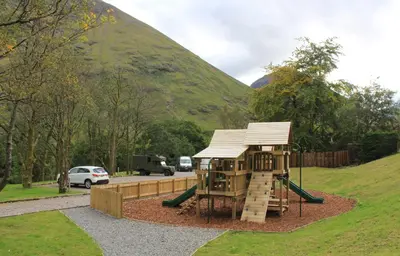 a playground in a park next to a mountain at Oak Tree Lodge in Ballachulish