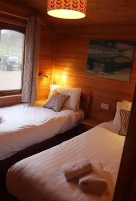 two beds in a room with wooden walls at Rowan Tree Lodge in Glencoe
