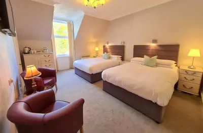 a hotel room with two beds and a chair at Corriemar House in Oban