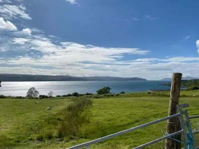 a field with a fence and a body of water at White Watch in Lochaline