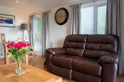 a living room with a brown leather couch and a table at Super King Lodge-Sleeps 2-HotTub-Sea View in Langbank