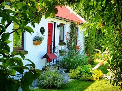 a white house with a red door and some plants at Haagwood Cottage in Cretshengan