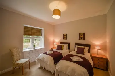 a bedroom with two beds and a chair and a window at Blairquhan Cottages in Maybole
