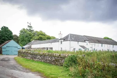 a white house with a stone wall and a barn at Coachmans Bothy - 50m from the beach in Port Appin