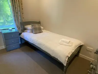 a small bed with white sheets and a blue dresser and a window at Puffin - Bach in Lerags