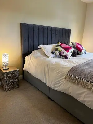 a bed with a blue headboard and pillows on it at Dunroamin in Drymen