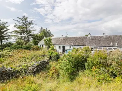a white house on a hill with tall grass at Grebe Cottage in Oban