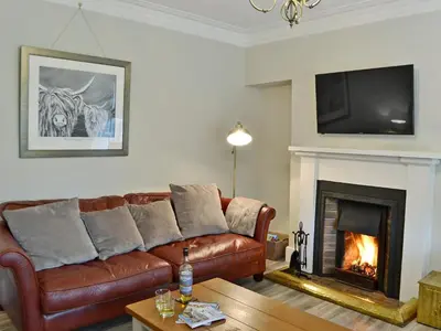 a living room with a brown leather couch and a fireplace at Altbeg in Brodick