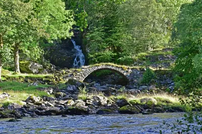 a stone bridge over a river with a waterfall at Gardeners Cottage in Chesthill