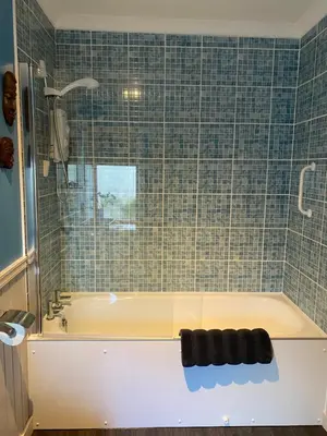 a bathroom with a tub and a tile wall at Holly Cottage in Glencoe