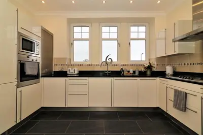a large kitchen with white cabinets and black tile floors at Signature - Greenlees Clubhouse 3 Bed in Cambuslang