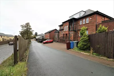 a street with houses and a fence and a red car at Signature - Greenlees Clubhouse in Glasgow