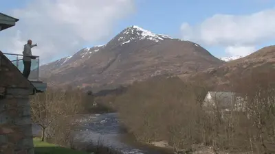 a man standing on a balcony looking at a mountain at Highland Getaway in Kinlochleven