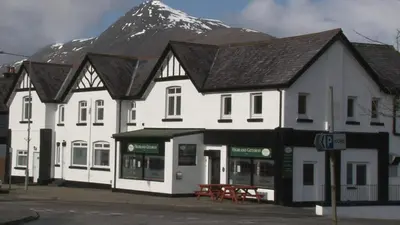 a large white building with a mountain in the background at Highland Getaway in Kinlochleven