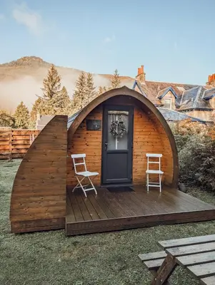 a small wooden cabin with two chairs on a deck at Strathyre Camping Pods in Strathyre