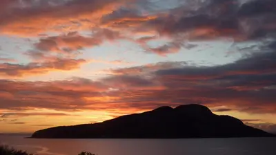a sunset over a mountain in the ocean with clouds at Kinneil Self Catering in Lamlash