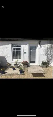 a white house with potted plants in front of it at GROOMS COTTAGE OUTSIDE HOT TUB in Beith