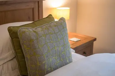 a bed with a green pillow and a wooden table at Sanaigmore Cottage in Port Charlotte